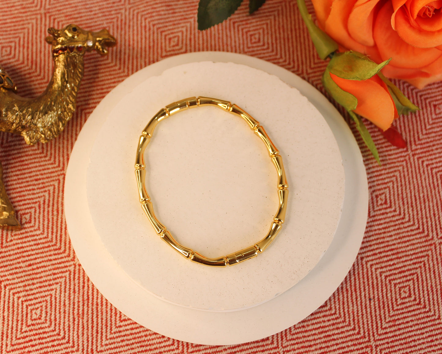 Gold bracelet on a white plate with an orange flower and decorative elements on a patterned red background