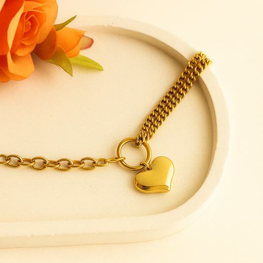 Gold bracelet with a heart charm on a beige plate with an orange rose.