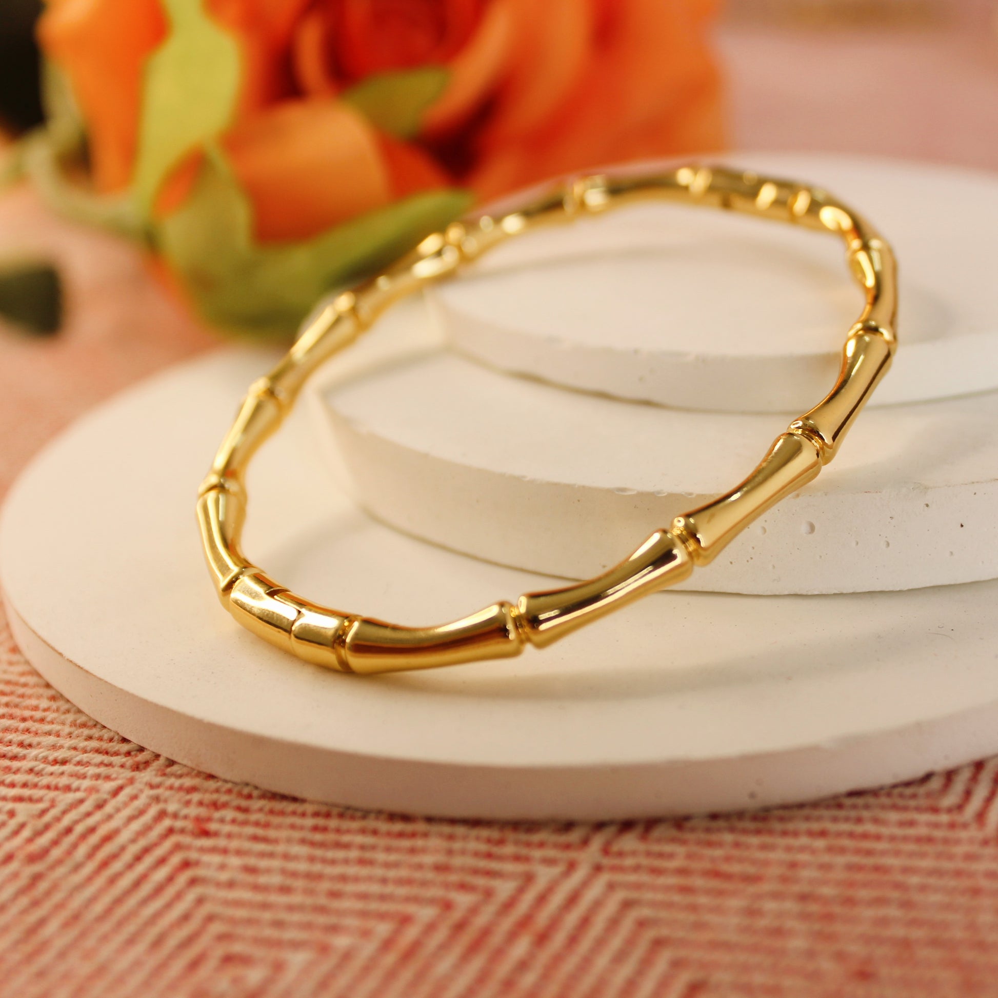Gold bracelet on a white surface with a blurred floral background