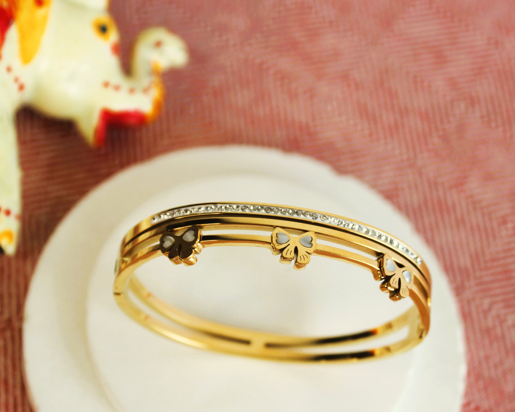 Gold bracelet with decorative elements on a white surface with a pink textured background